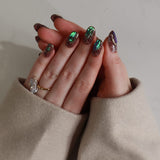Close-up of a hand with glittery nail polish and rings, wearing a beige sweater.