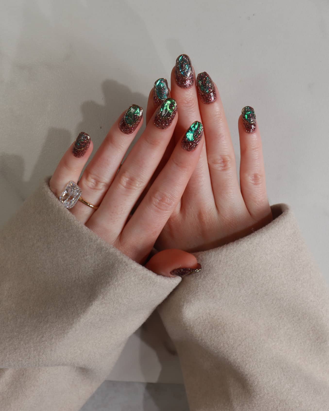 Close-up of hands with decorative nail art and a ring, wearing a beige sleeve.