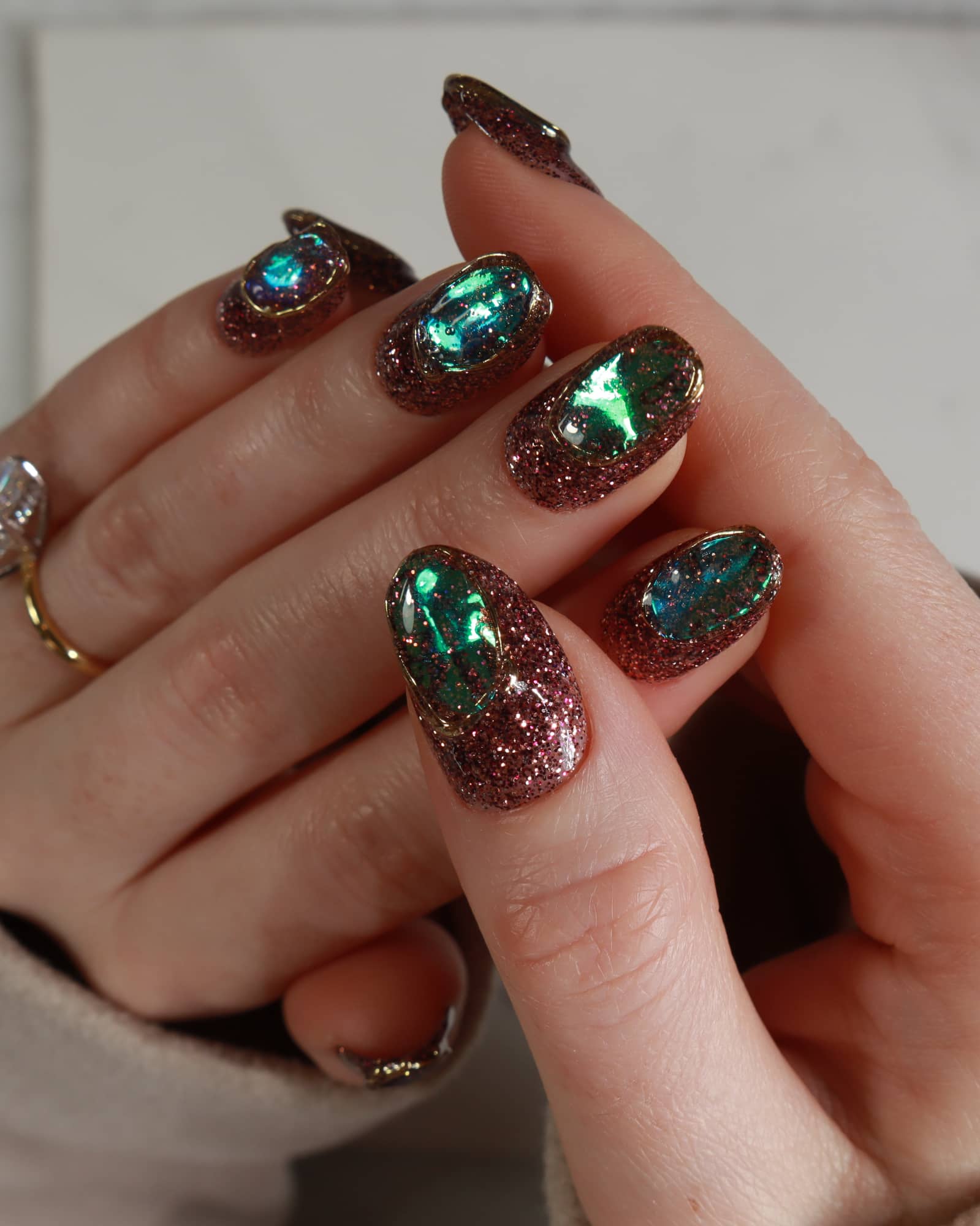 Hand with glittery, multicolored nail polish on a neutral background