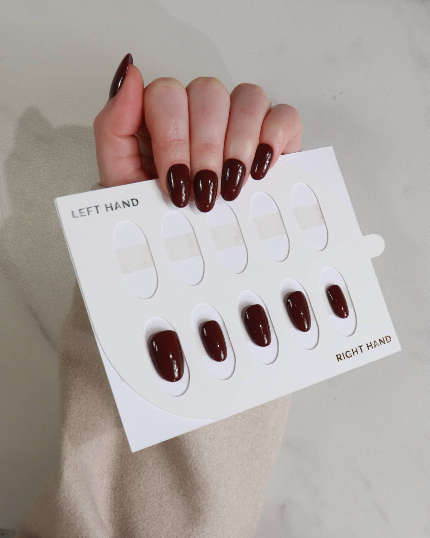 Nail polish samples on a card held by a hand with dark nail polish.