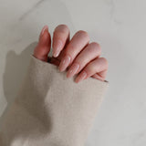 Close-up of a hand with pink nail polish holding a beige sleeve against a neutral background