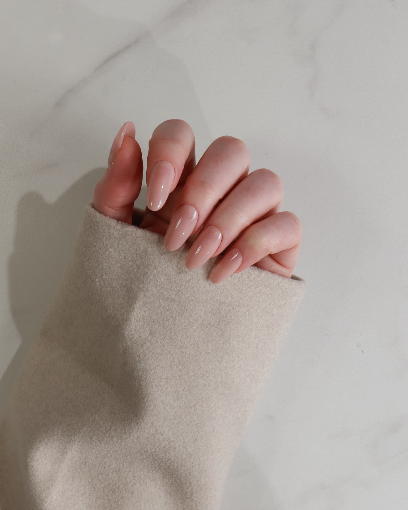 Close-up of a hand with pink nail polish holding a beige sleeve against a neutral background