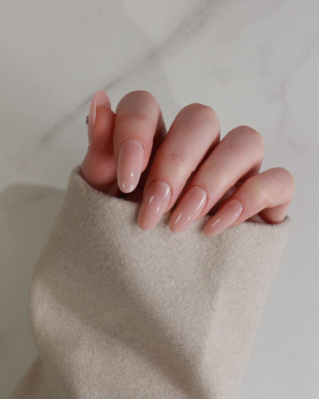 Close-up of a hand with nude nail polish on a neutral background