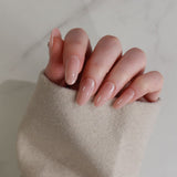 Close-up of a hand with nude nail polish on a neutral background