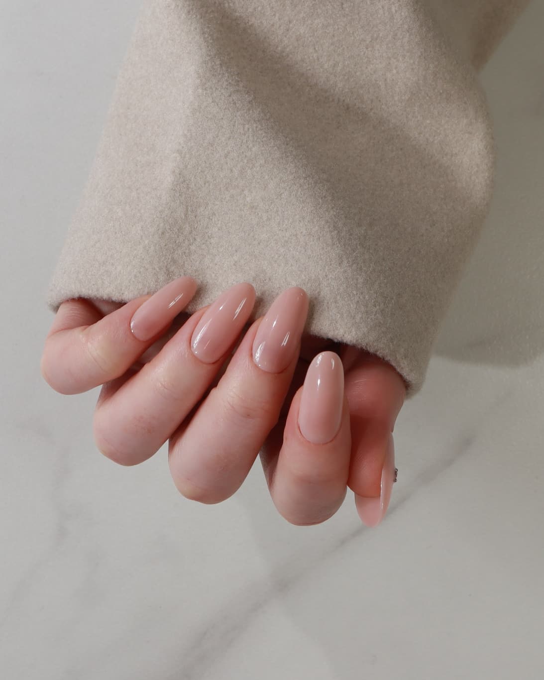 Hand with nude polish wearing a beige sweater on a neutral background