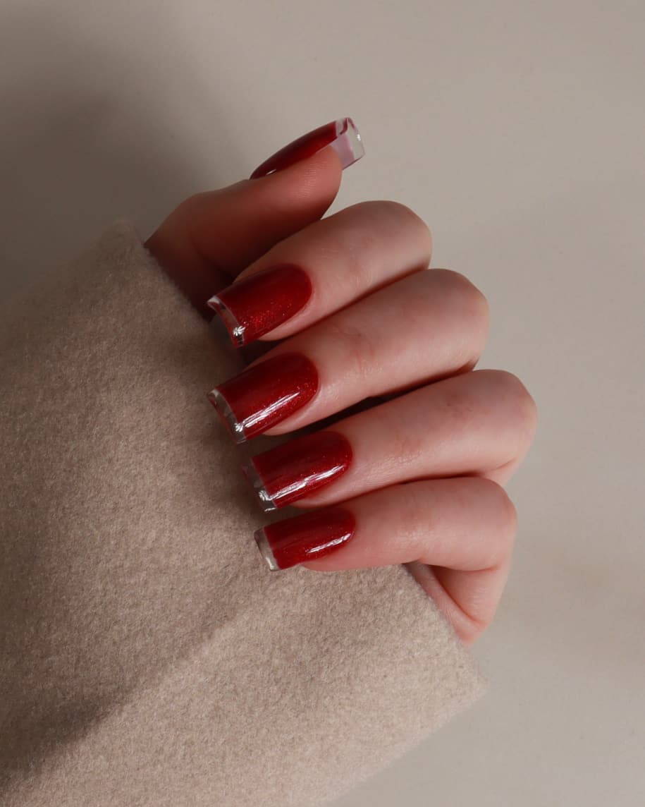 Hand with red nail polish wearing a beige sleeve on a neutral background