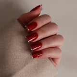 Hand with red nail polish wearing a beige sleeve on a neutral background