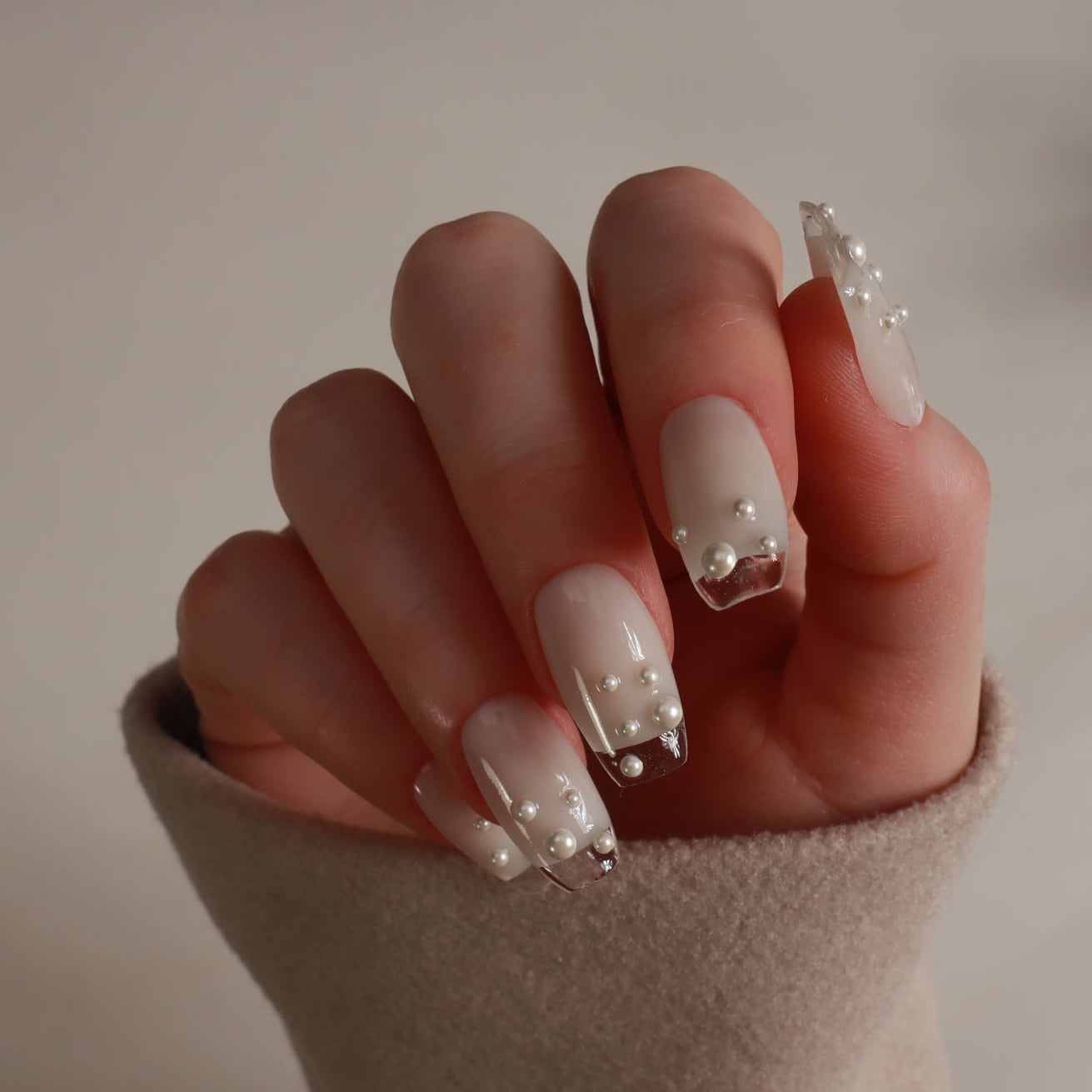 Hand with pearl and crystal nail design against a neutral background