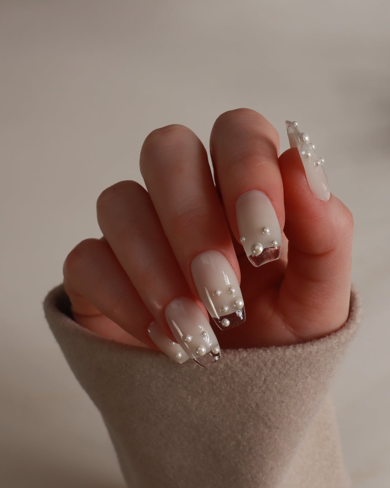 Hand with pearl and crystal nail design against a neutral background