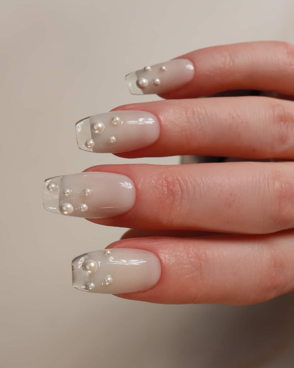 Hand with clear nail polish and embedded pearls on a neutral background
