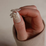 Hand holding a delicate silver ring with pearls against a neutral background