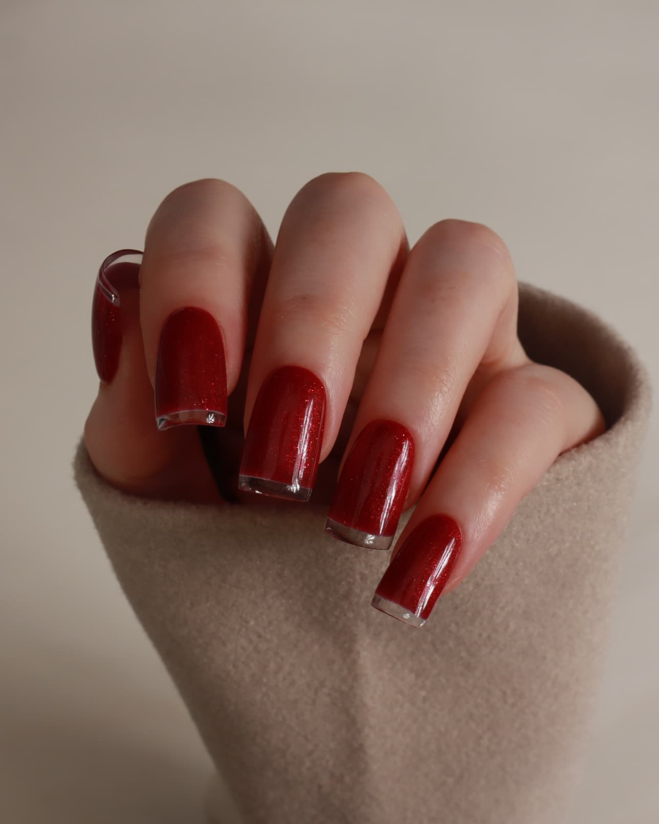 Hand with red nail polish on a neutral background