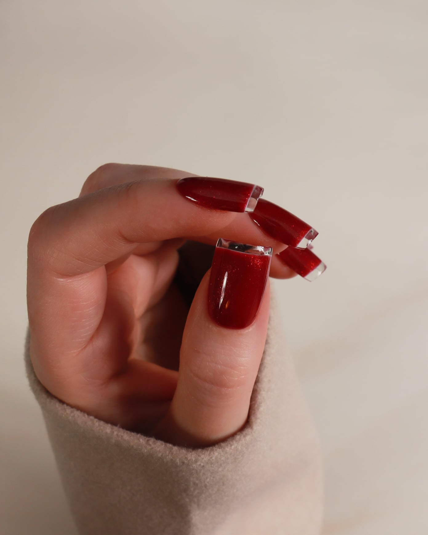 Hand with red nail polish holding a small object against a plain background