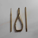 Set of gold-colored tools including a pair of cuticle nippers, cuticle pusher, and cuticle loop on a light gray background.