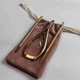 Gold nail tools on a pink velvet pouch with a logo on a light gray background