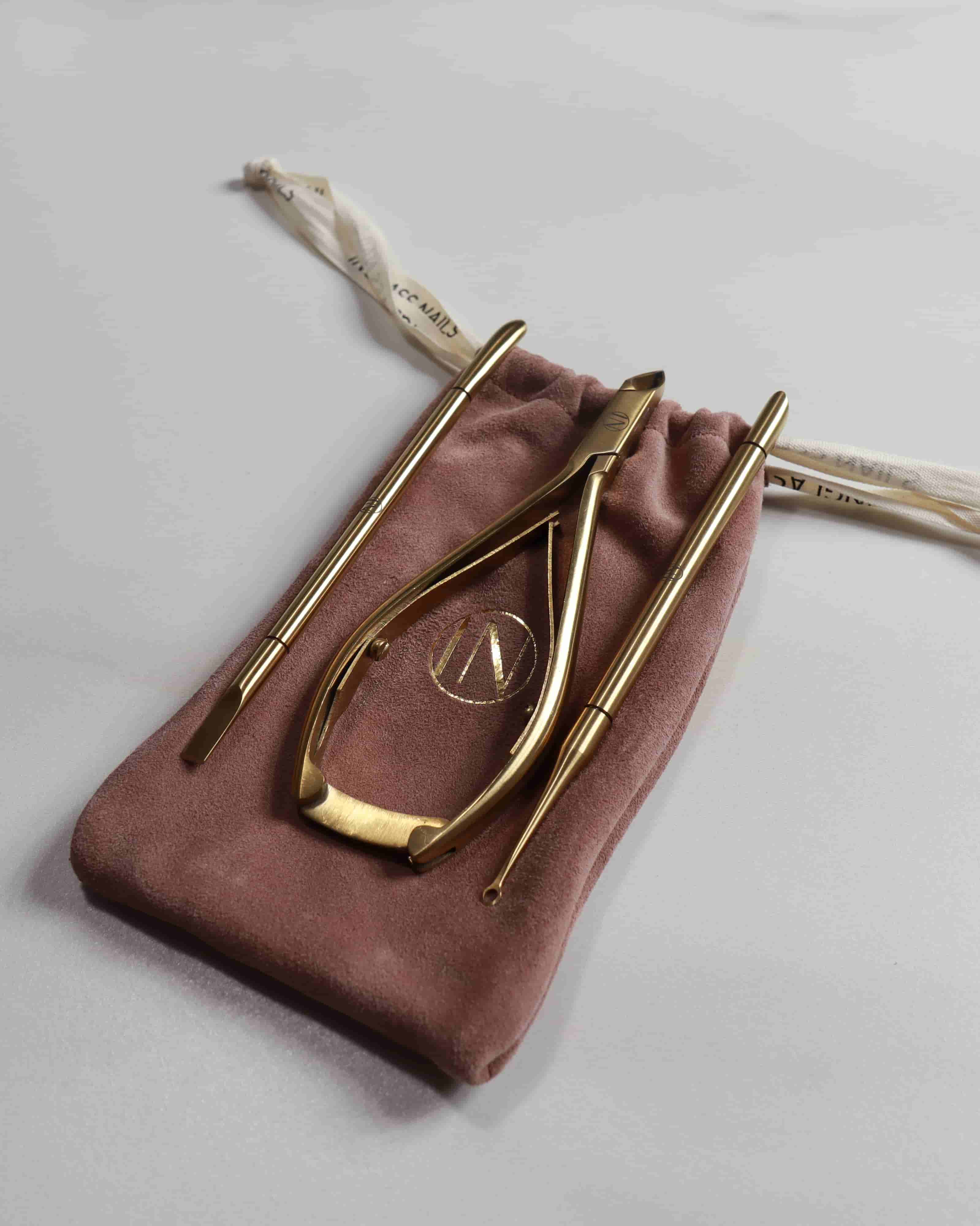 Gold nail tools on a pink velvet pouch with a logo on a light gray background