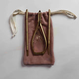 Set of gold nail care tools on a pink drawstring bag against a light gray background