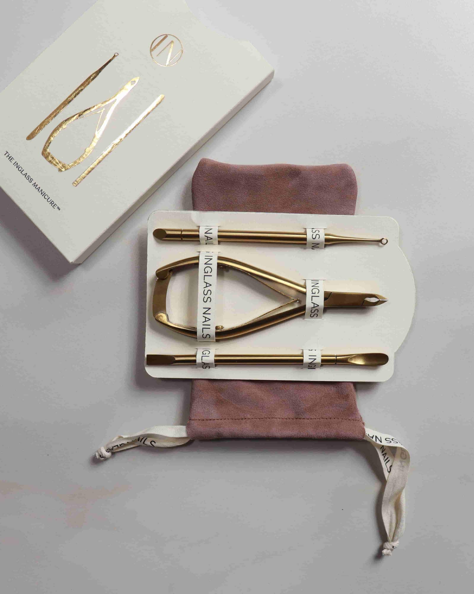 Set of gold nail tools with a branded box on a gray surface