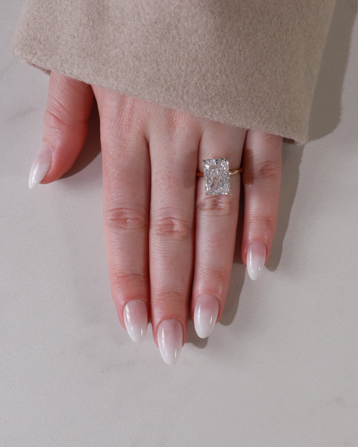 Hand wearing a diamond ring on a neutral background
