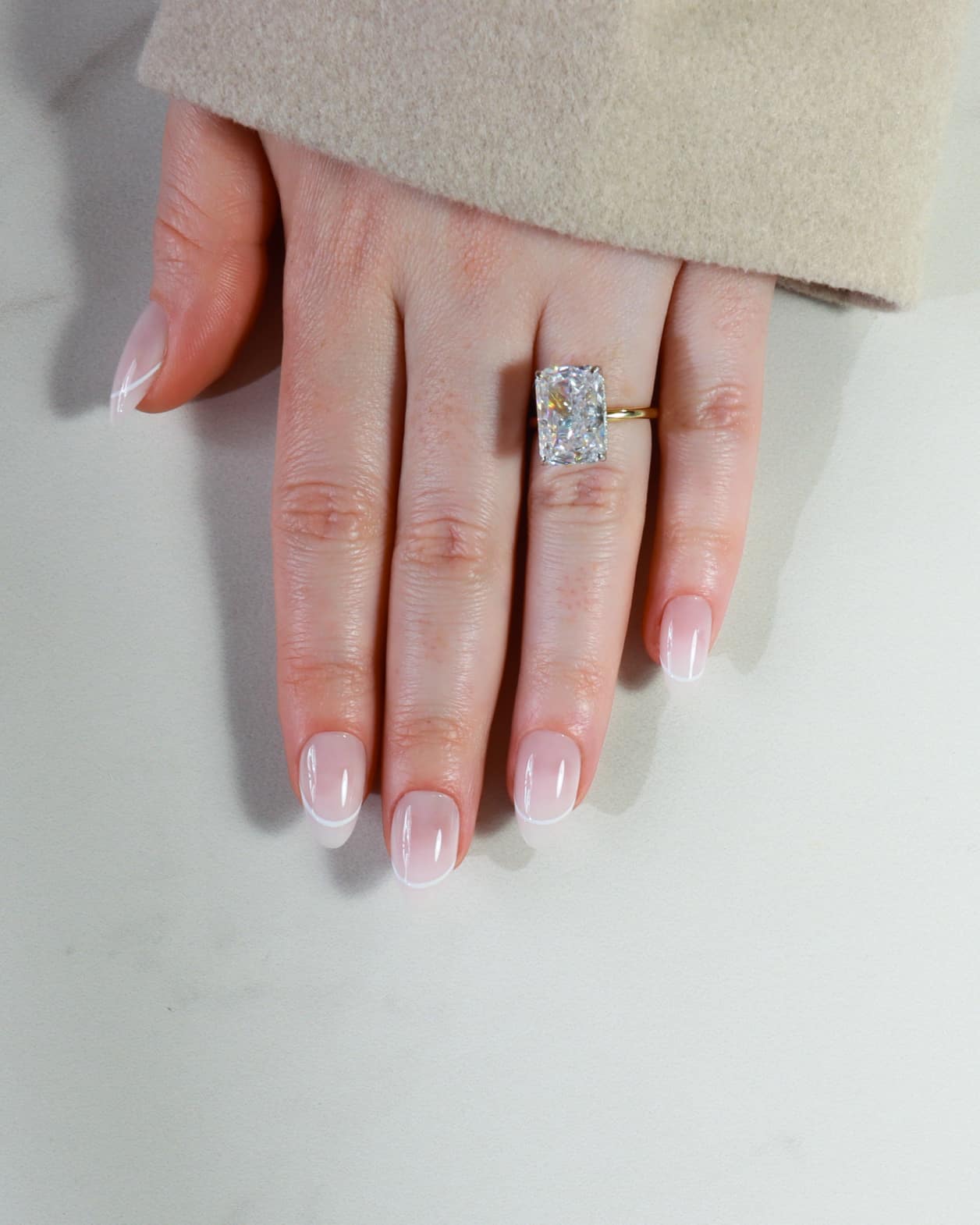 Hand wearing a diamond ring on a plain background