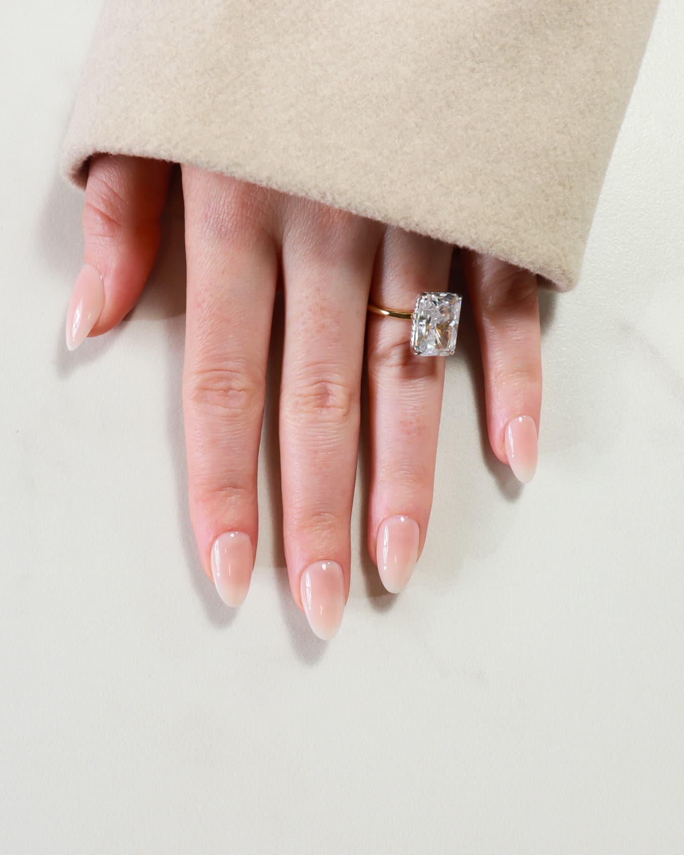 Hand wearing a diamond ring on a neutral background