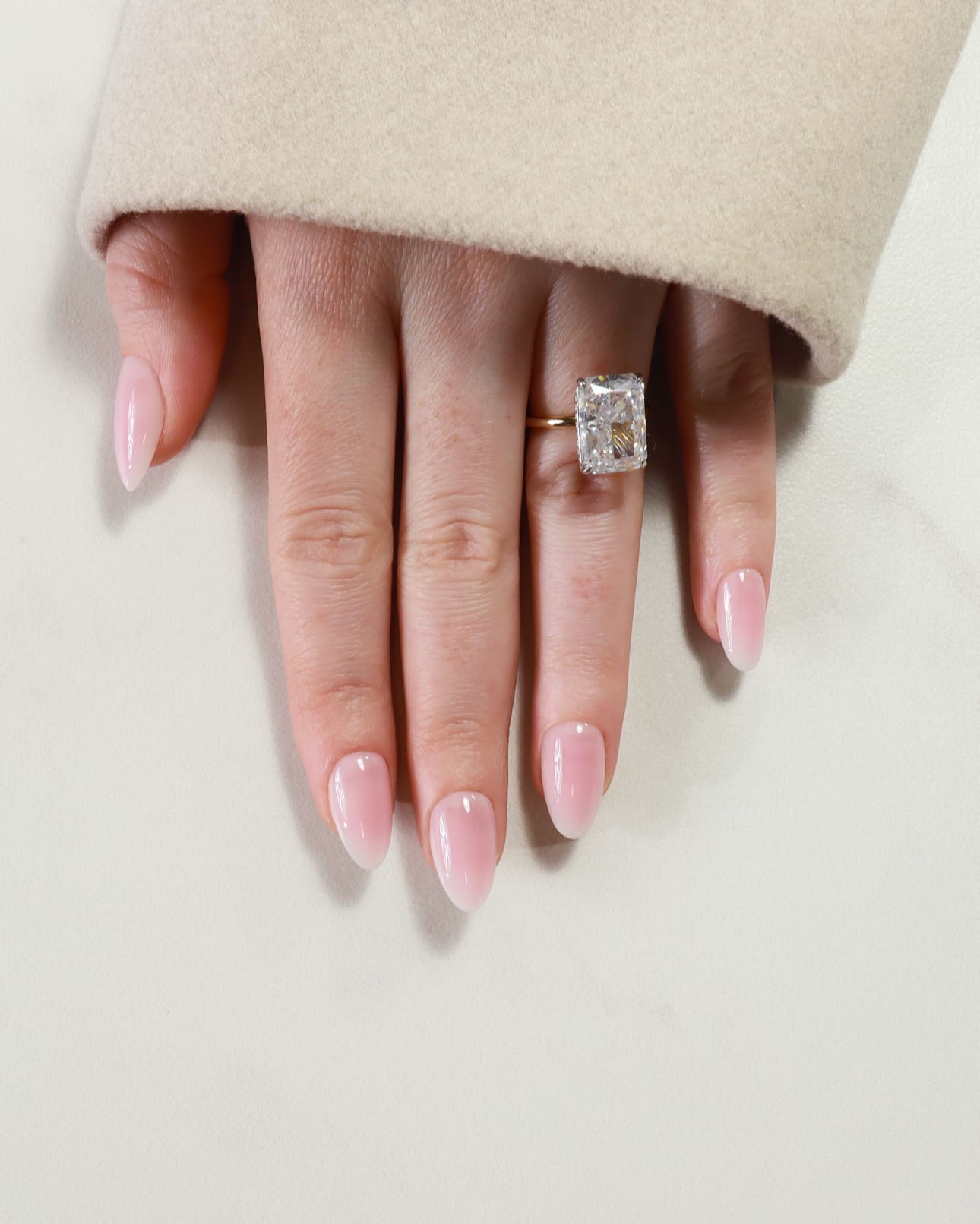 Hand wearing a diamond ring on a neutral background