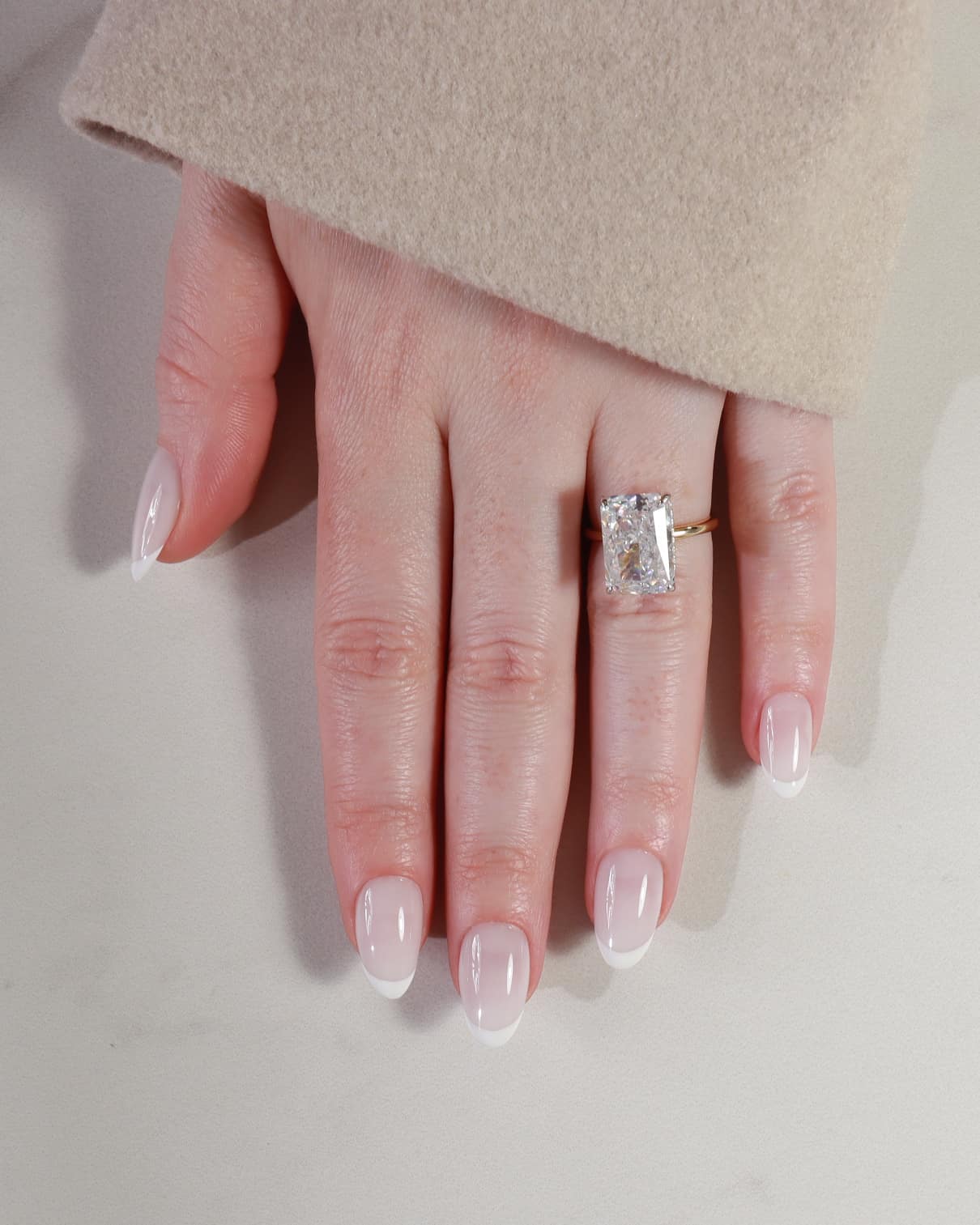 Hand wearing a diamond ring on a neutral background