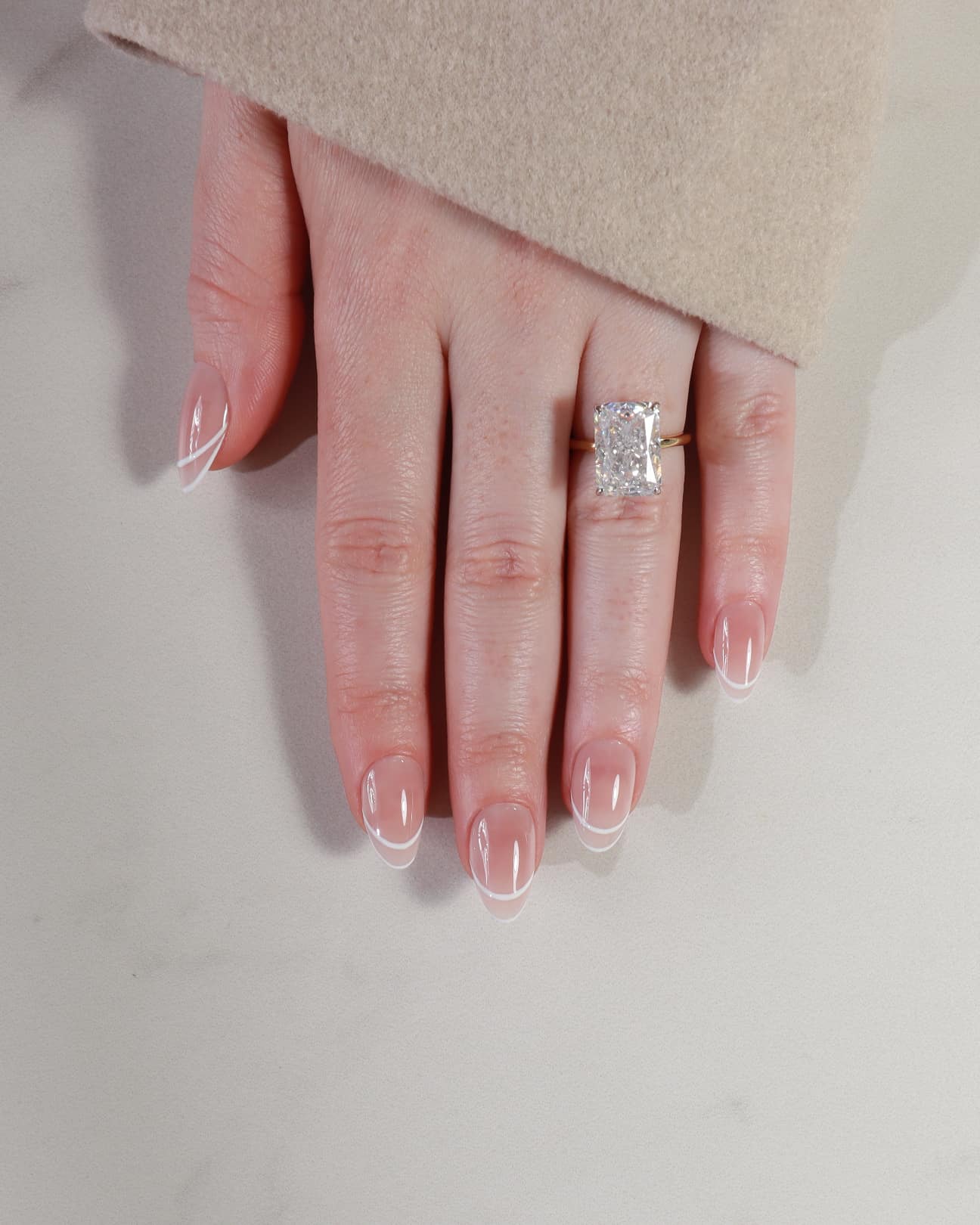 Hand wearing a diamond ring on a neutral background