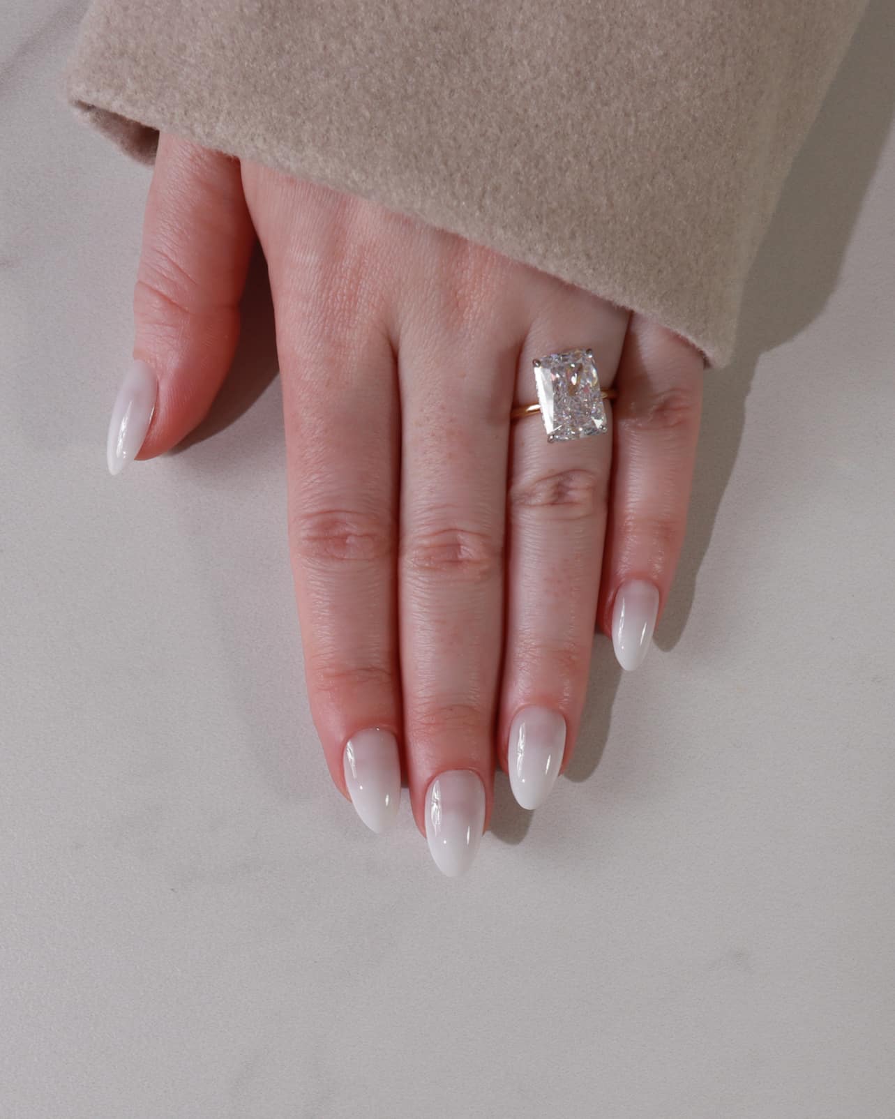 Hand wearing a diamond ring on a neutral background with shade in1 ombre