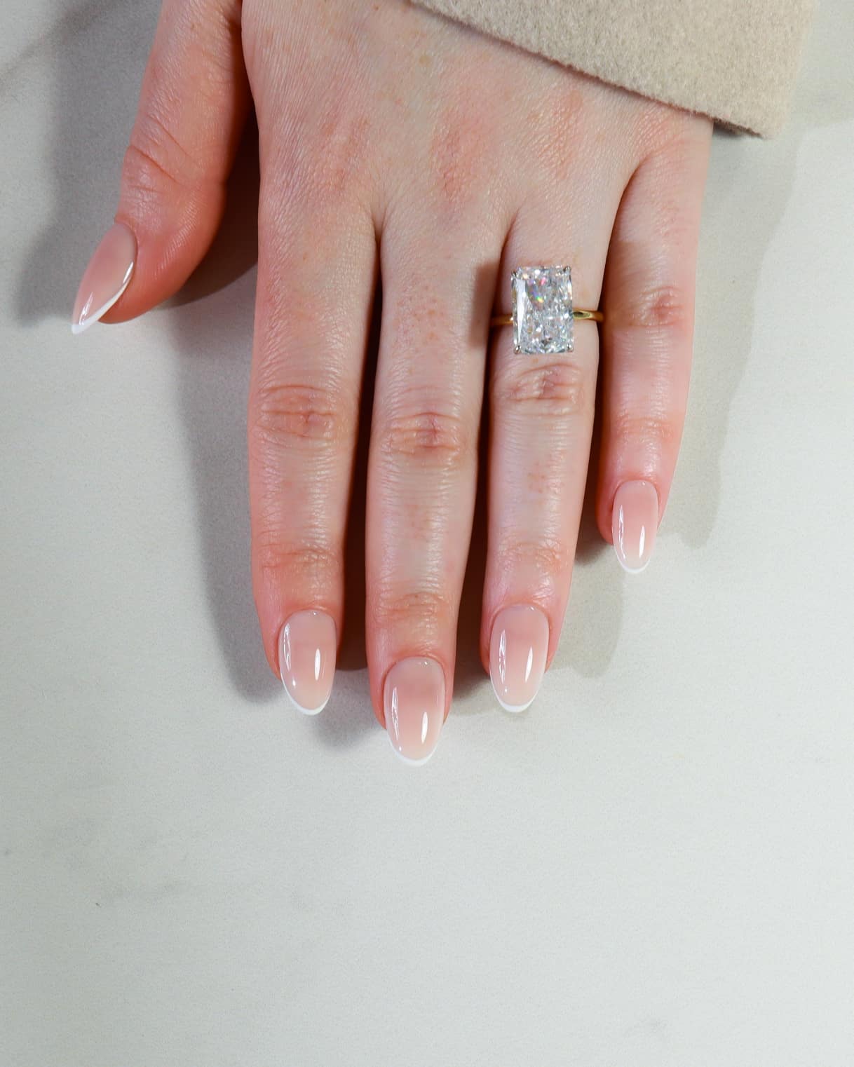 Hand wearing a diamond ring on a neutral background