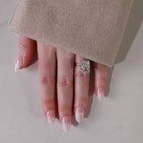Hand wearing a diamond ring with beige coat sleeve on a neutral background