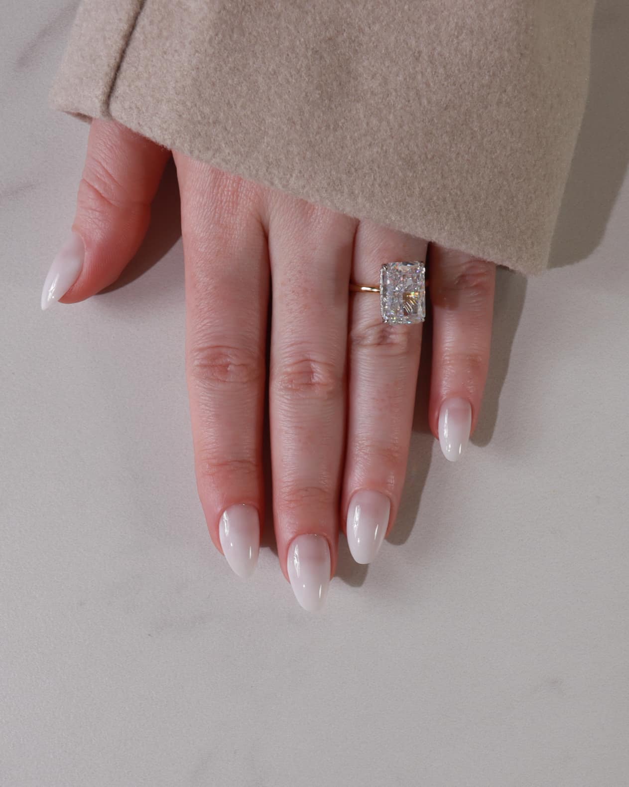 Hand wearing a diamond ring on a neutral background with shade in05
