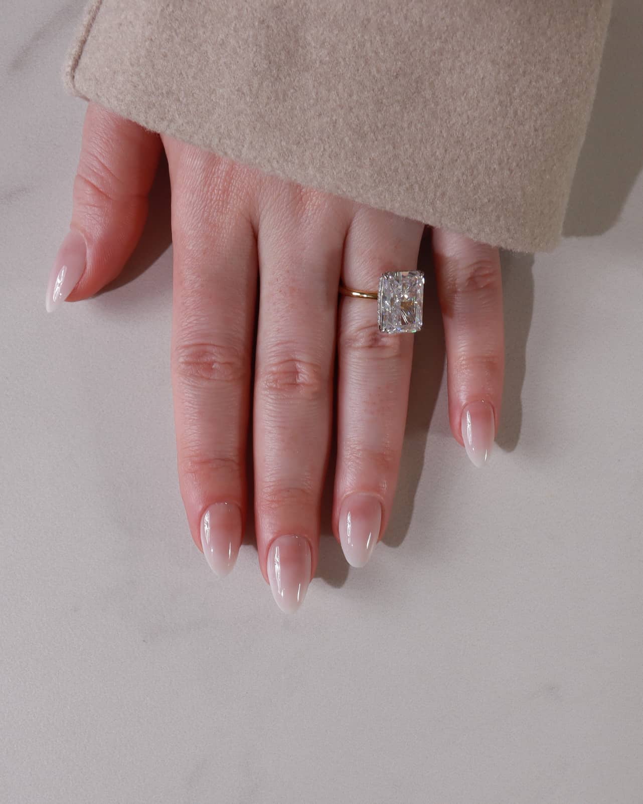 Hand wearing a diamond ring on a neutral background with shade in06