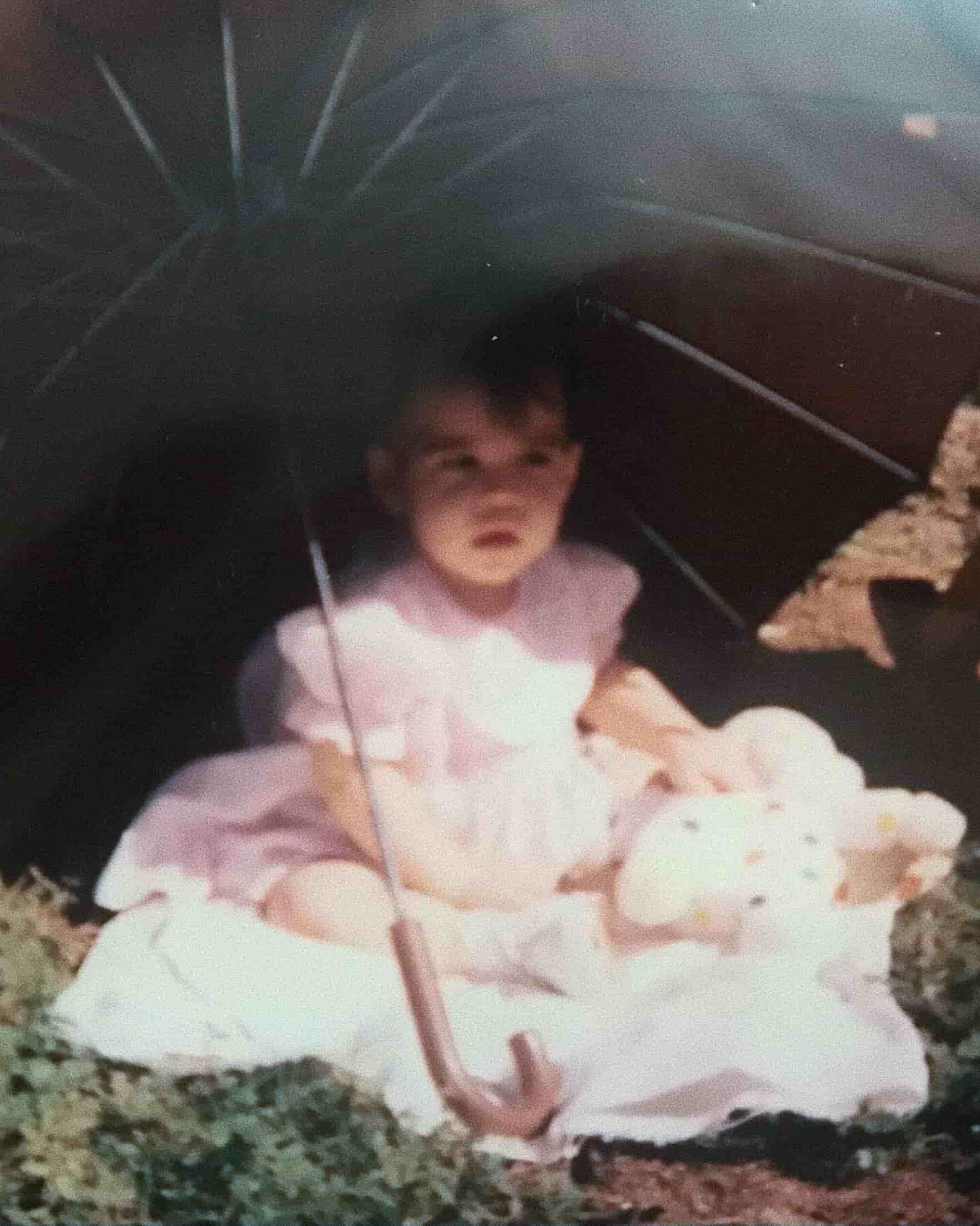Child in a pink dress holding a teddy bear under an umbrella